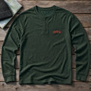 Alaska State Upside Down embroidery design stitched on a forest green long-sleeve henley