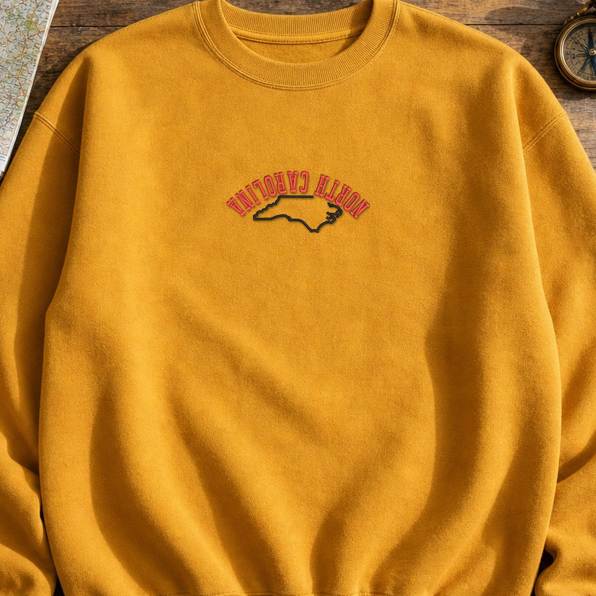 North Carolina State Upside Down embroidery design stitched on a warm gold crewneck sweatshirt